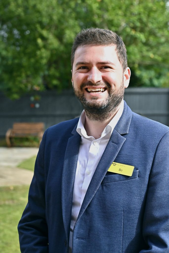 man in a shirt and jacket smiling outdoors