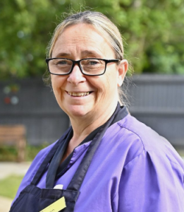 woman with hair in ponytail wearing a purple shirt and apron