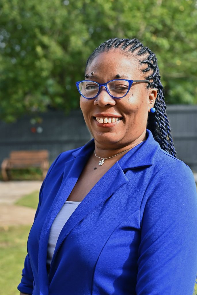 woman in blue blazer and glasses smiling outdoors